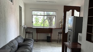 Amplia sala de estar con un sofá de cuero negro, una mesa de comedor de madera y un televisor integrado.