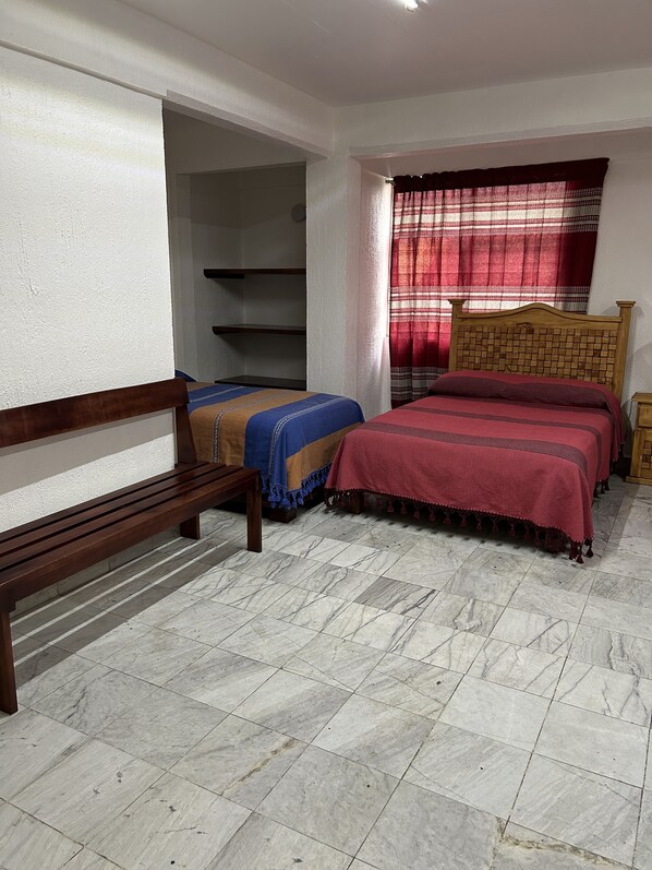 A bedroom with two beds, a wooden bench, and a wardrobe. - Habitaciones Leonor (Oaxaca)