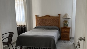 Un dormitorio con cama, una silla, una mesita de noche con lámpara y una puerta con cerradura de llave.