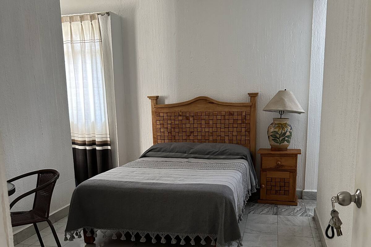 A bedroom with a bed, a chair, a nightstand with a lamp, and a door with a key lock.