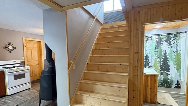 Eine Holztreppe führt zu einer oberen Ebene, einem Küchenbereich mit Herd und einer Tür mit Vorhängen mit Waldmotiv.