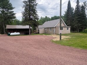 Une allée de gravier mène à une maison dont le toit est en métal, et qui est entourée d’arbres.