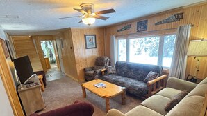 Ein gemütliches Wohnzimmer mit Holzboden, Deckenventilator, einer Couch, einem Sessel, einem Couchtisch und einem Fernseher.