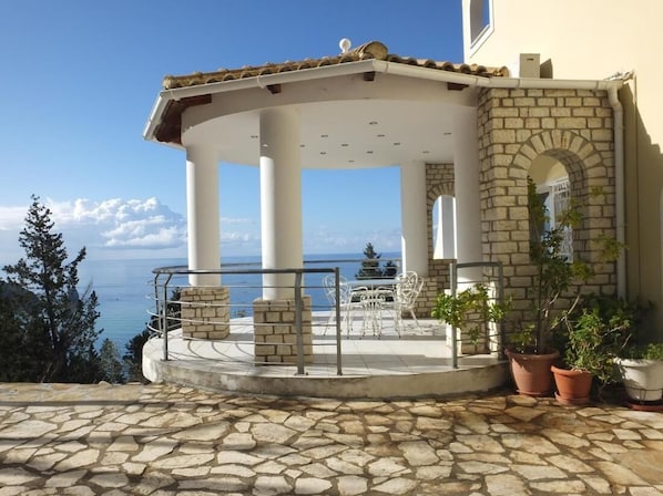 Enjoy the serene sea views from this outdoor space with a stone floor, potted plants, and comfortable seating.