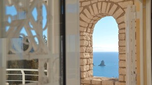 A stone archway leading to a balcony with a view of the sea and a distant island. - Villa Alibertini With sea View (Corfu)