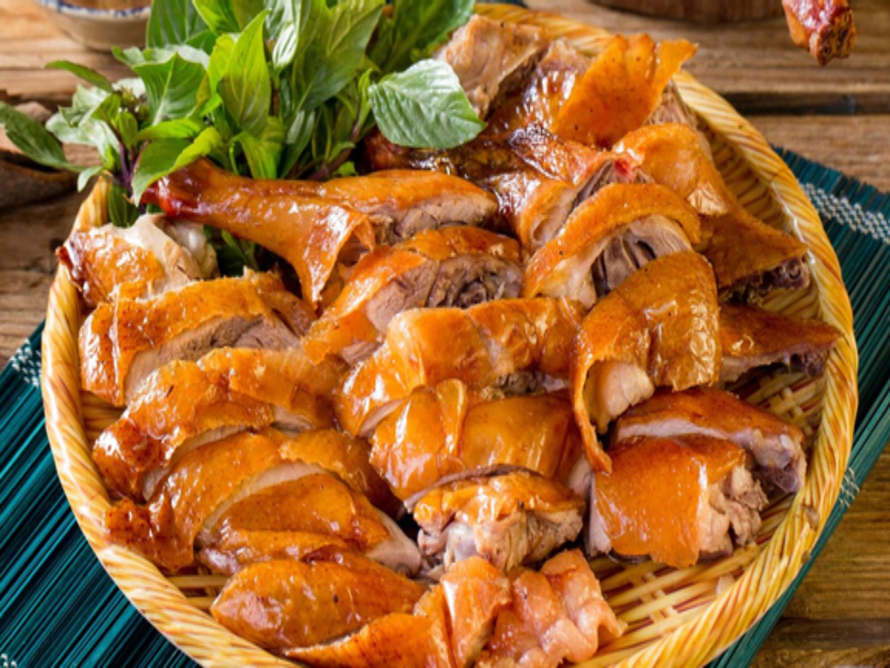 Un panier de canard rôti à la peau croustillante, garni de feuilles vertes.