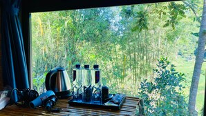 Una mesa de madera con una tetera, botellas y una bandeja en una habitación con vista a un bosque denso a través de una ventana.