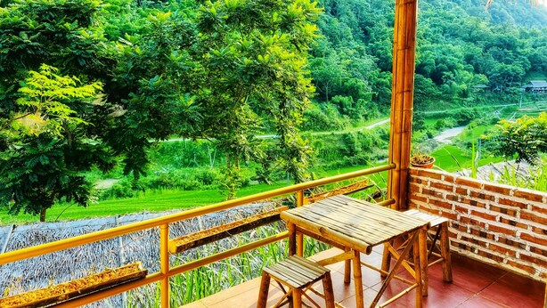 Un balcón con mesa y banco de madera, con vista a un valle verde exuberante con campos en terrazas y un río.