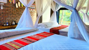 Una habitación con dos camas, cada una con ropa de cama blanca y un corredor estampado rojo. La habitación presenta una pared de ladrillo y un ventanal con vistas a zonas verdes.