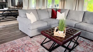 A modern living room with a grey sectional sofa, red and white cushions, a wooden coffee table with a plant, and a patterned rug. - Townside@LavaHotSprings (Lava Hot Springs)