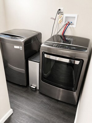 A compact, modern laundry room with a built-in washer and dryer, a small step for access, and a power outlet with cables.