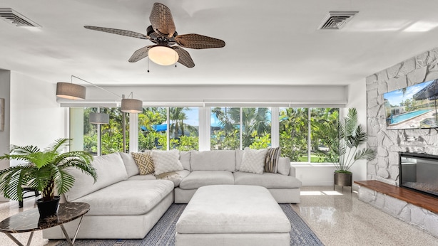 A modern living room with a sectional sofa, a coffee table, a fireplace, and large windows with a view of greenery. - Siesta Dolce | Private Pool, Kayaks and Putting Green (Siesta Key)