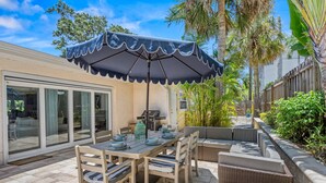 An outdoor patio with a dining table, chairs, and a large umbrella. - Siesta Dolce | Private Pool, Kayaks and Putting Green (Siesta Key)