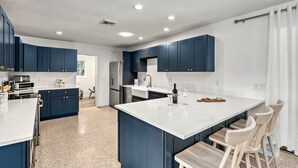 A modern kitchen with dark blue cabinets, a white marble island, and a seating area with wooden chairs. - Siesta Dolce | Private Pool, Kayaks and Putting Green (Siesta Key)