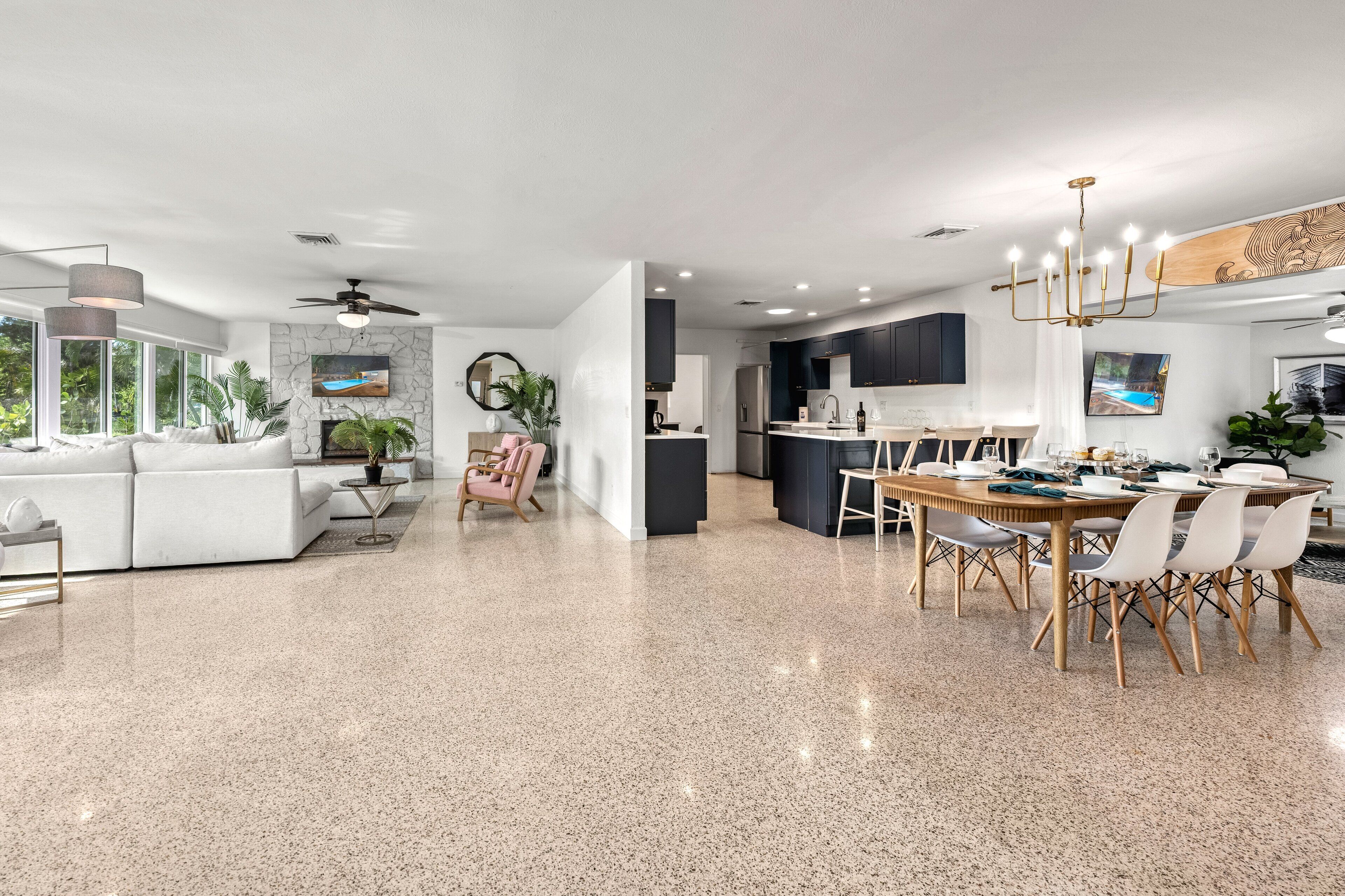 A spacious living room with a white sofa, a dining area with a wooden table and chairs, and a kitchen with dark cabinets and a white countertop.