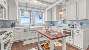 Une cuisine moderne avec des meubles blancs, une table en bois et des luminaires suspendus.