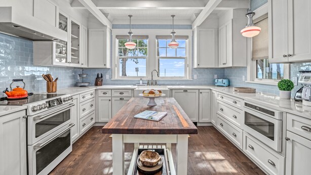 Une cuisine moderne avec des meubles blancs, un îlot central en bois et une vue sur l’extérieur.