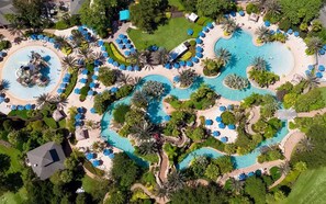 Vue aérienne d’un complexe hôtelier doté de plusieurs piscines, de chaises longues et de palmiers.