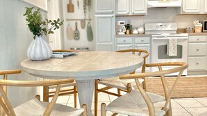A modern kitchen with white cabinets, a round wooden dining table, and wicker chairs. - The Coconut (Cocoa Beach)