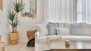 A living room with a white sofa, striped pillows, a woven side table, and a potted plant. - The Coconut (Cocoa Beach)