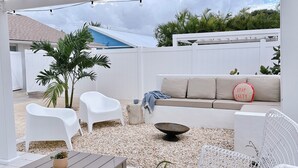 An outdoor patio with a covered seating area, white furniture, and a decorative bowl. - The Coconut (Cocoa Beach)