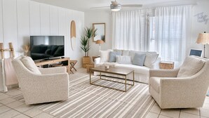 A modern living room with a flat-screen TV, white sofas, a coffee table, and a striped rug. - The Coconut (Cocoa Beach)