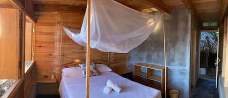 Habitación de cabaña de madera con cama, mosquitero y un pequeño estante de madera.