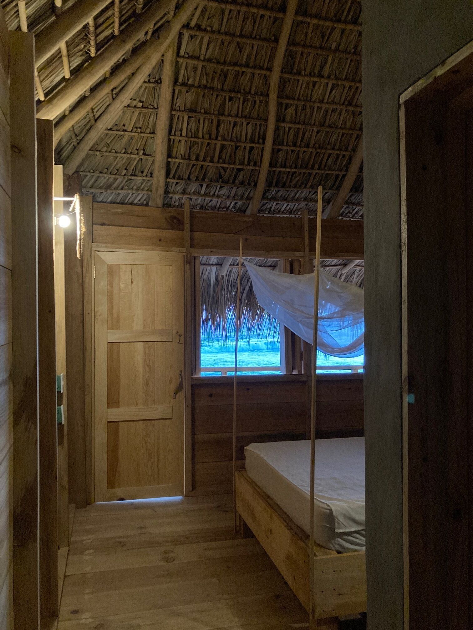 Una camera in legno con un letto, una finestra dotata di zanzariera e una porta in legno.