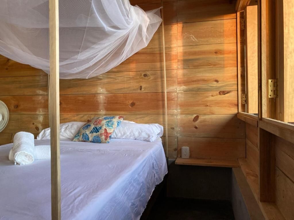 A wooden cabin room with a bed, a mosquito net, and a small shelf.