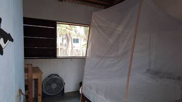 Una habitación con una cama, una mesa de madera, un ventilador y una ventana con vista a palmeras.