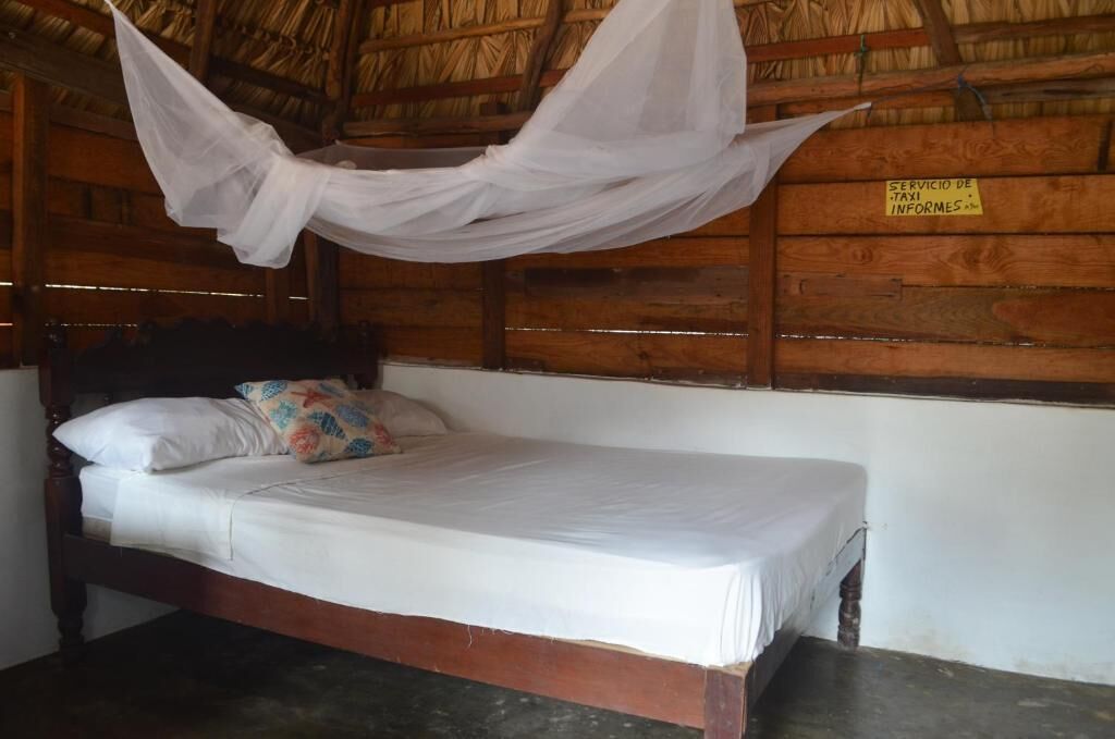 A single bed in a wooden room with a thatched roof, a mosquito net above the bed, and a sign on the wall.