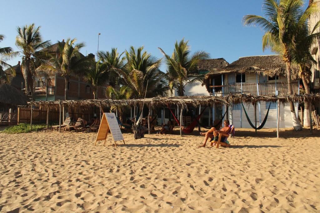 A beach with thatched-roof huts, palm trees, and a wooden chair.