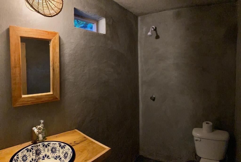A bathroom with a wooden vanity, a small window, a toilet, and a shower area.