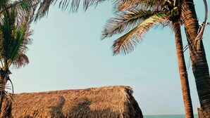 Una playa con una cabaña de techo de paja, palmeras y una hamaca.
