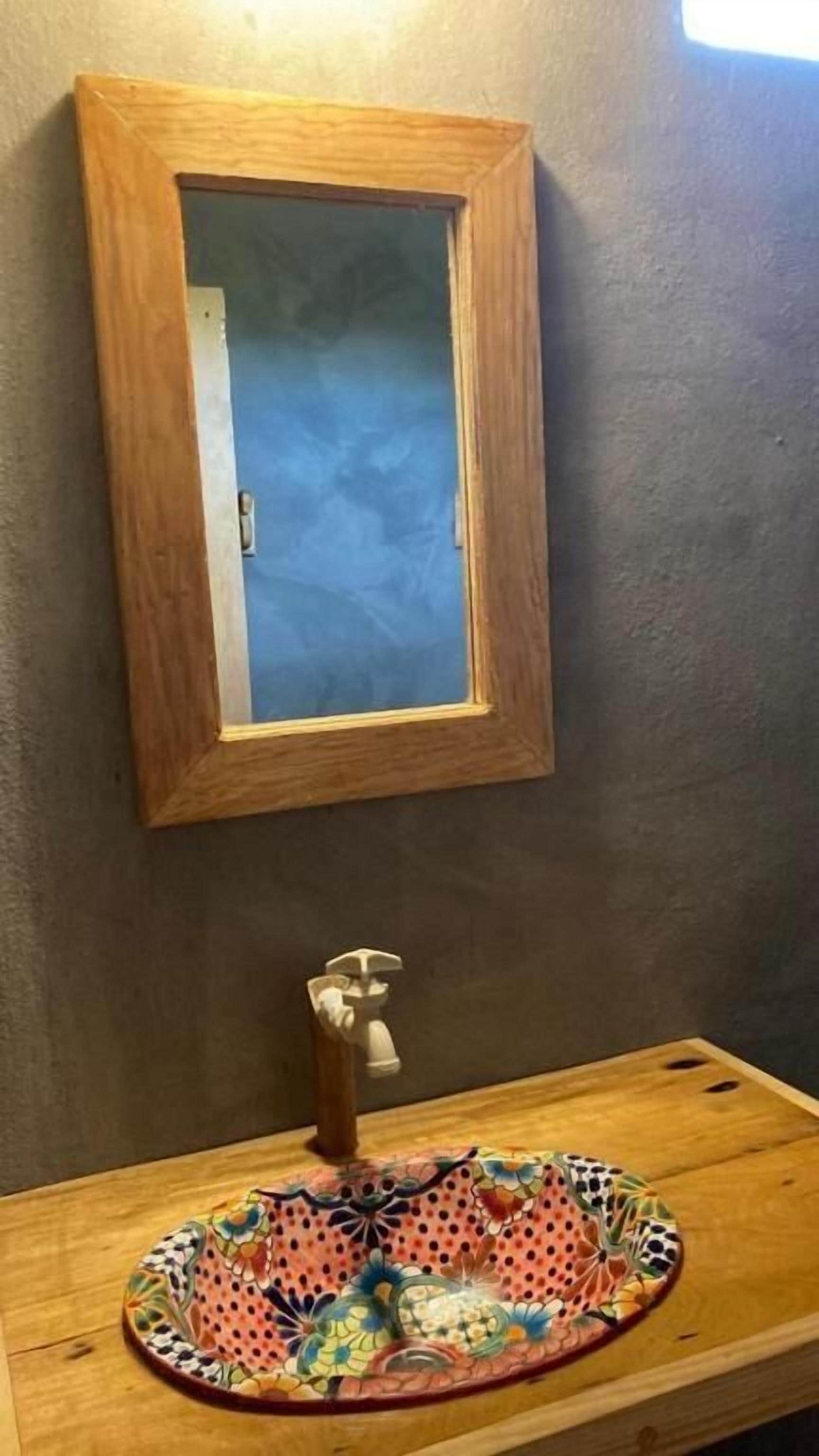 A wooden-framed mirror above a wooden sink with a colorful, patterned basin.