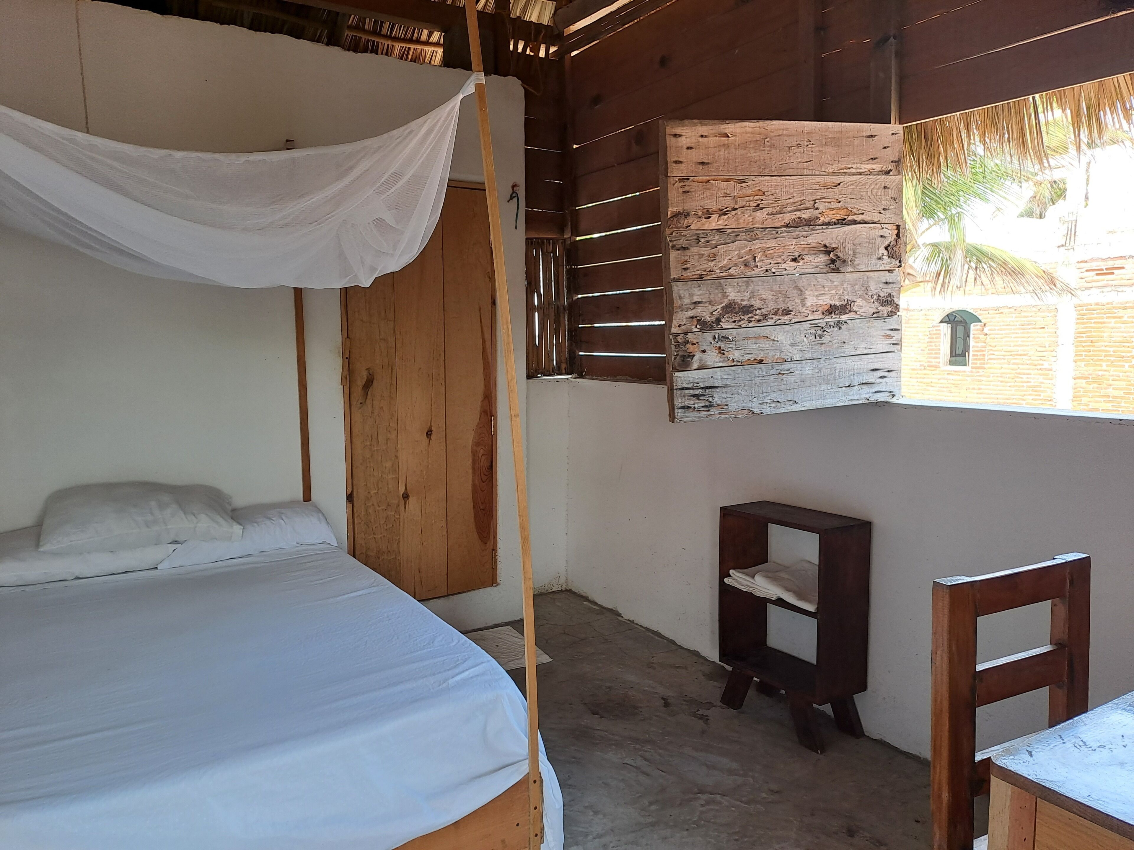Una stanza con un letto, un armadio in legno, un piccolo tavolino e una finestra vista esterna.