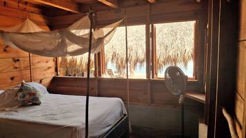 Habitación de cabaña de madera con cama, mosquitero y ventilador.