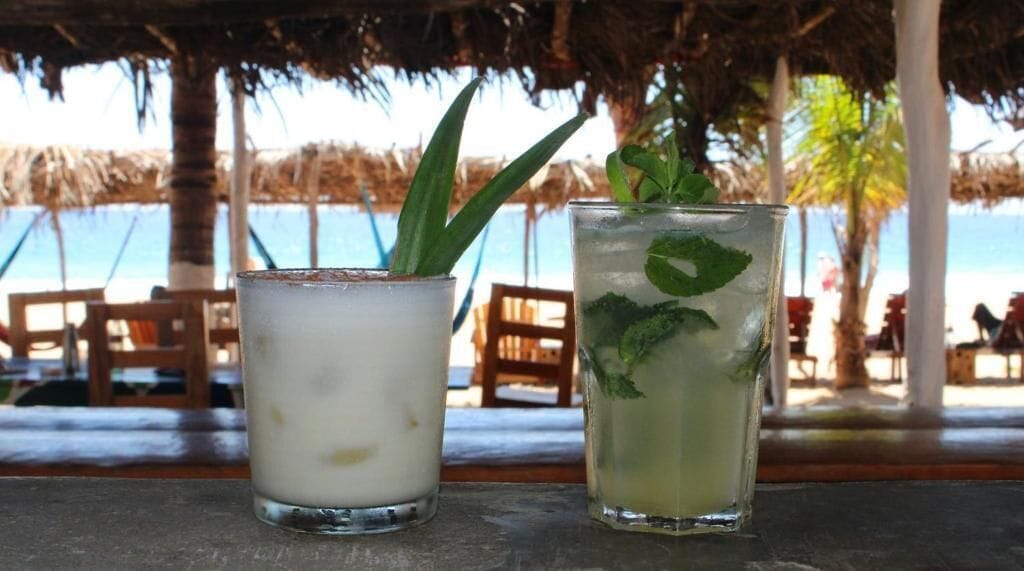 Two drinks on a table with a beach view in the background.
