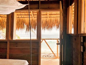 A wooden room with a bed, a window with a view of the beach, and a thatched roof. - Ballelita (San Pedro Pochutla)
