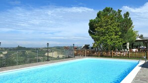 A rectangular swimming pool with a stone border, surrounded by a metal fence and a wooden fence. - Nice apartment for 2 people with WIFI, pool, A/C, terrace, pets allowed and panoramic view (Vinchio)