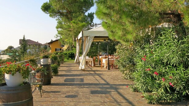 A paved pathway leading to a covered outdoor seating area with tables and chairs, surrounded by greenery and potted plants. - Nice apartment for 2 people with WIFI, pool, A/C, terrace, pets allowed and panoramic view (Vinchio)