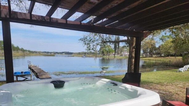 Ein Whirlpool unter einer Holzpergola mit Blick auf einen See und einen Steg.