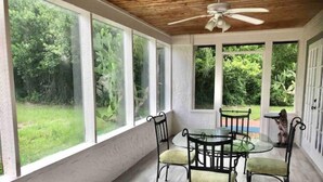 Eine überdachte Terrasse mit Glastisch und Stühlen, großen Fenstern und einem Deckenventilator.