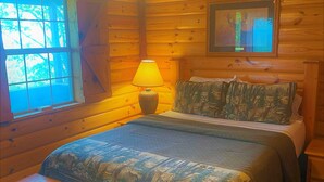 A wooden cabin bedroom with a bed, a nightstand, a lamp, a dresser, and a ceiling fan. - Deer Run is your perfect Mountaintop Cabin Equipped for Family Adventure! (Mena)
