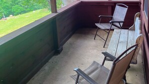 A covered porch with wooden walls and a view of a red-roofed building and green trees. - Deer Run is your perfect Mountaintop Cabin Equipped for Family Adventure! (Mena)