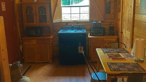 A cozy cabin-style kitchen with wooden walls, a large window, a refrigerator, and a dining table with chairs. - Deer Run is your perfect Mountaintop Cabin Equipped for Family Adventure! (Mena)