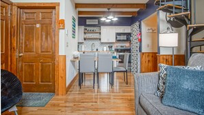 A compact kitchen with wooden cabinets, a dining area with chairs, and a staircase.