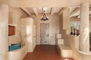 A hallway with a wooden ceiling, a chandelier, a door with a grid pattern, and a bench.