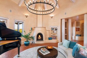 A spacious living room with a fireplace, a grand piano, and a modern chandelier.