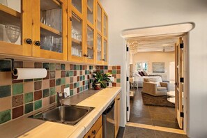 A kitchen with a tiled backsplash, wooden cabinets, a stainless steel sink, and a dining area with a sofa and a table.